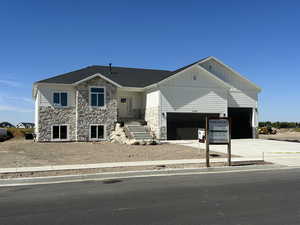 View of front facade featuring stone siding, board and batten siding, driveway, and a garage