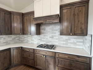 Kitchen with decorative backsplash, light stone counters, ventilation hood, vaulted ceiling, and stainless steel gas cooktop