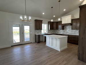 Kitchen with backsplash, dark brown cabinetry, light wood-style floors, lofted ceiling, and hanging light fixtures