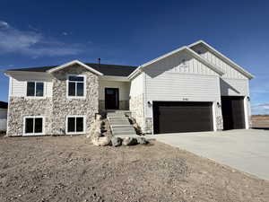 View of front facade with stone siding, board and batten siding, driveway, and a garage