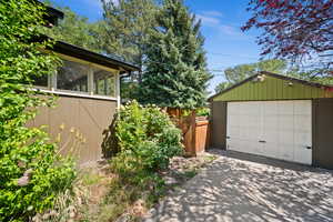 View of property exterior with concrete driveway, a garage, an outdoor structure, and a sunroom