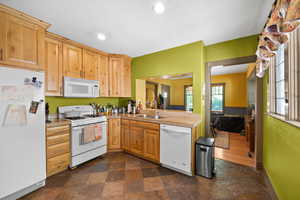 Kitchen featuring white appliances, dark stone finish floors, light brown cabinets, recessed lighting, and a peninsula