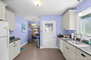Kitchen with freestanding refrigerator, decorative light fixtures, dark countertops, and white cabinetry