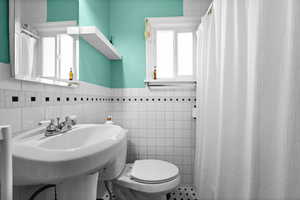 Full bathroom with a wainscoted wall, tile walls, and curtained shower