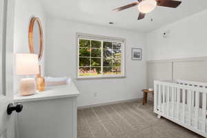 Carpeted bedroom with a nursery area, ceiling fan, and wainscoting