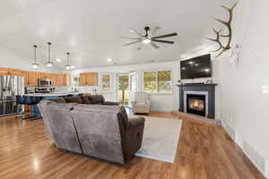 Living area with vaulted ceiling, ceiling fan, a tiled fireplace, wood finished floors, and recessed lighting