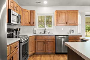 Kitchen with appliances with stainless steel finishes, light countertops, light wood-type flooring, recessed lighting, and brown cabinetry