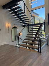 Stairway with a towering ceiling, wood finished floors, and arched walkways