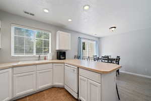 Kitchen featuring white dishwasher, a peninsula, healthy amount of natural light, recessed lighting, and white cabinets