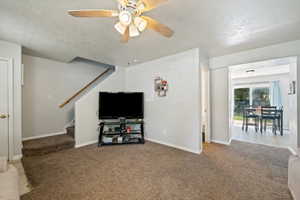 Carpeted living room with stairs, ceiling fan, and a textured ceiling