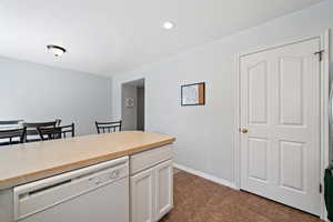 Kitchen with white dishwasher, white cabinetry, light countertops, recessed lighting, and dark tile patterned floors