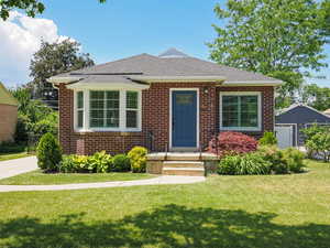 Bungalow-style house featuring brick siding, a shingled roof, and a front lawn