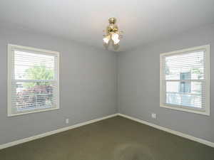 Unfurnished room featuring healthy amount of natural light, dark colored carpet, and a ceiling fan