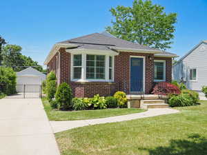 Bungalow with brick siding, a front lawn, an outbuilding, a shingled roof, and a garage