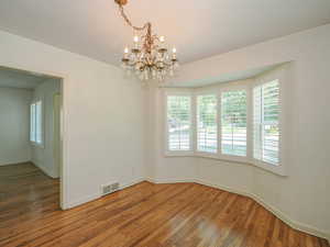 Empty room with plenty of natural light, a chandelier, and wood finished floors
