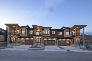 Contemporary house featuring a balcony, a garage, driveway, and stone siding