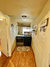 Corridor featuring washer and dryer, a textured wall, wood finished floors, and a textured ceiling