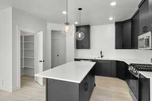 Kitchen featuring stainless steel appliances, dark cabinetry, light wood-style flooring, and recessed lighting