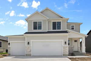 Craftsman-style home featuring stone siding, driveway, and a garage