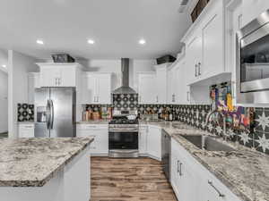 Kitchen with stainless steel appliances, wall chimney exhaust hood, dark wood-style flooring, decorative backsplash, and recessed lighting