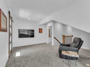Living area featuring an upstairs landing, carpet, a barn door, and recessed lighting