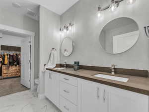 Bathroom featuring double vanity, marble finish flooring, and a spacious closet