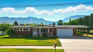 Single story home with an attached garage, a mountain view, concrete driveway, a chimney, and brick siding