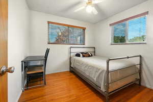 Bedroom with light wood finished floors, multiple windows, a textured ceiling, and a ceiling fan