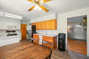 Kitchen with white appliances, a ceiling fan, wood finished floors, light countertops, and white cabinetry