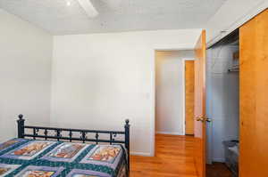 Bedroom with wood finished floors, a textured ceiling, a closet, and a ceiling fan