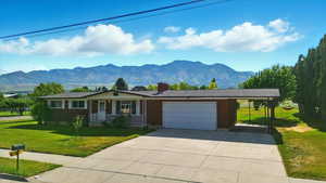Single story home featuring covered porch, a garage, a mountain view, and a front lawn