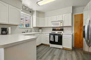Kitchen featuring white appliances, wood finished floors, white cabinets, and light countertops