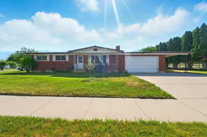 Ranch-style home with a garage, brick siding, covered porch, driveway, and a front lawn