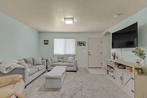 Living room with light colored carpet, a textured ceiling, light tile patterned flooring, and arched walkways