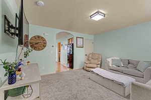 Living area with arched walkways, a textured ceiling, and carpet