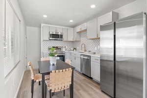 Kitchen with stainless steel appliances, decorative backsplash, gray cabinetry, light wood finished floors, and recessed lighting