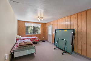 Carpeted bedroom featuring a textured ceiling and wooden walls