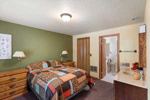 Carpeted bedroom featuring ensuite bath and a textured ceiling