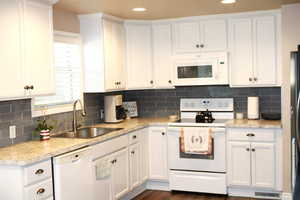 Kitchen with white appliances, light countertops, white cabinets and subway tile back splash.
