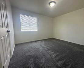 Empty room featuring dark carpet and baseboards
