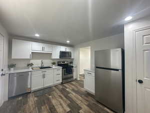 Kitchen with appliances with stainless steel finishes, dark wood-style flooring, recessed lighting, white cabinets, and light stone counters