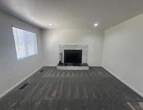 Unfurnished living room featuring dark colored carpet, a stone fireplace, and recessed lighting