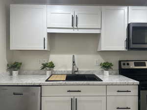Kitchen with stainless steel appliances, white cabinets, and light stone countertops