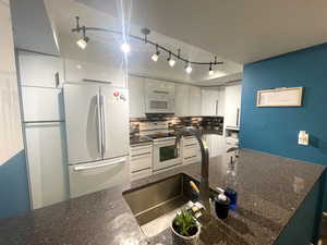 Kitchen with white appliances, rail lighting, white cabinets, tasteful backsplash, and dark stone countertops