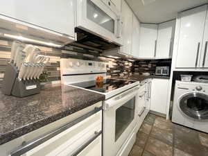Kitchen with white appliances, washer / dryer, white cabinetry, and backsplash