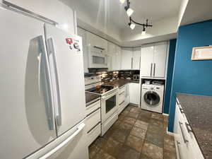 Kitchen featuring white appliances, washer / dryer, white cabinets, backsplash, and stone finish flooring