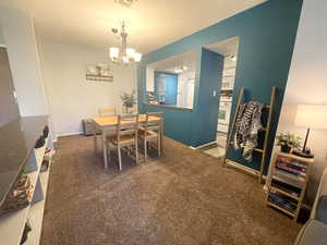 Carpeted dining area with a chandelier and baseboards