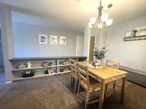 Dining space with dark colored carpet and a chandelier