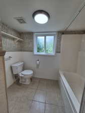 Bathroom featuring tile walls, tile patterned flooring, shower / washtub combination, and wainscoting