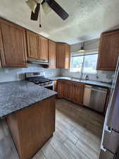 Kitchen featuring stainless steel appliances, under cabinet range hood, brown cabinetry, a ceiling fan, and wood tiled floors